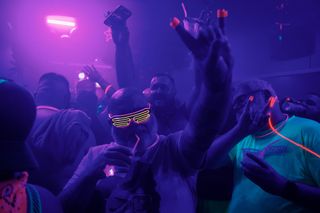 A group of men wearing glowing clothing and accessories dancing in a club