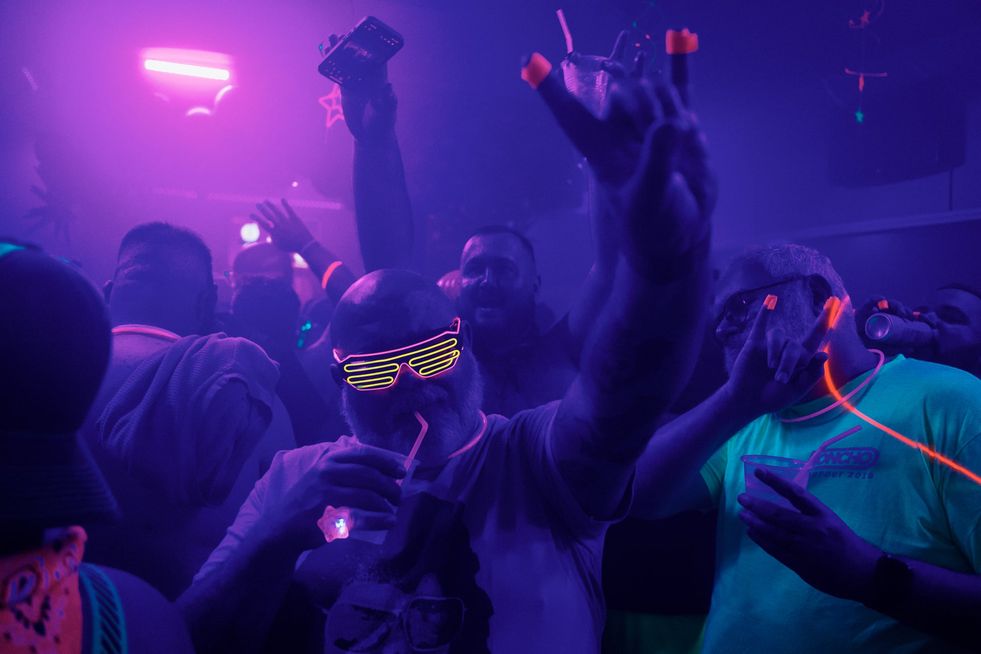 A group of men wearing glowing clothing and accessories dancing in a club