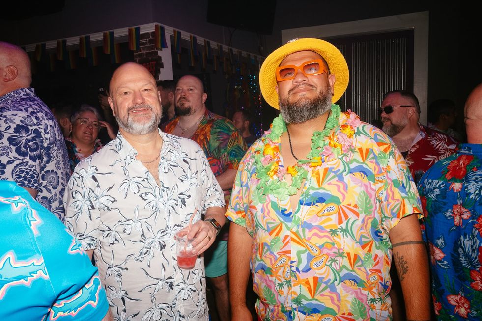 Two men in a club surrounded by others, wearing Hawaiin shirts and beach apparel