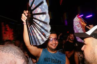 A man in sunglasses excitedly waving a fan on the dance floor