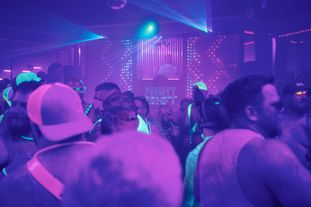 A large group of people wearing glowing clothing and accessories dancing in a club