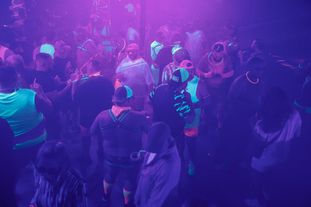 A large group of people wearing glowing clothing and accessories dancing in a club