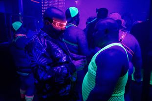A group of men wearing glowing clothing and accessories dancing in a club