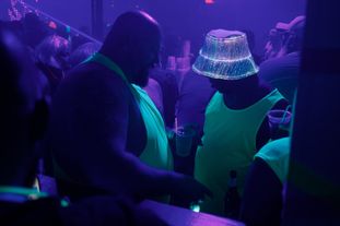 A group of men wearing glowing clothing and accessories dancing in a club