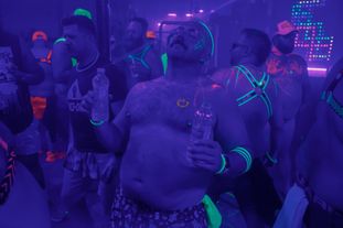 A group of men wearing glowing clothing and accessories dancing in a club