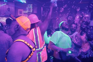A large group of people wearing glowing clothing and accessories dancing in a club
