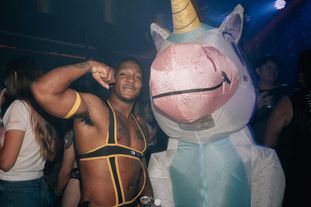 A go-go dancer flexes, posing with a person in an inflatable unicorn costume