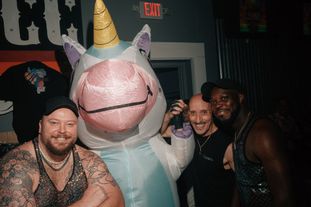 A group of people in a club pose for the camera with a person wearing an inflatable unicorn costume