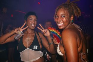 Two women on the dance floor. One making peace signs with her hands, her diamond tooth makes a star shape from the flash
