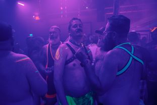 A group of men wearing glowing clothing and accessories dancing in a club