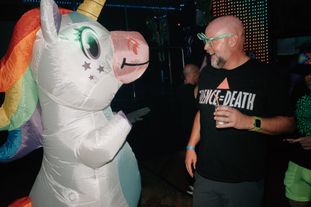 A man smiling at another person in an inflatable unicorn costume
