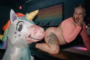 A person in an inflatable unicorn costume has his 'nose' on a go-go dancers butt