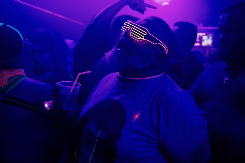 A bearded man singing and dancing in a club wearing glowing shutter shade glasses