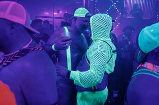 A group of men wearing glowing clothing and accessories dancing in a club