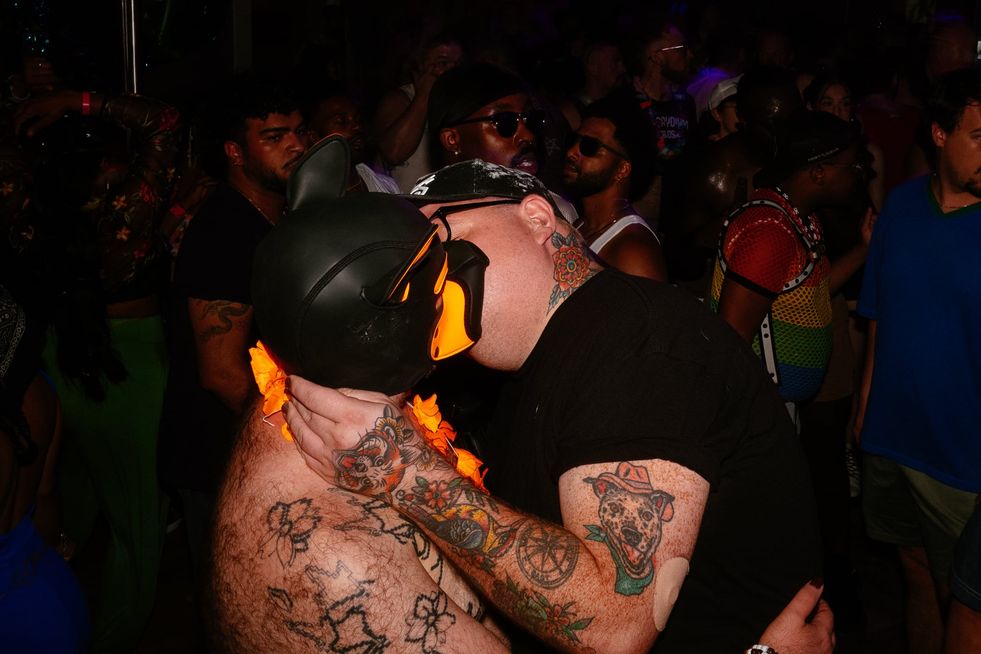 A tattooed man making out with another tattooed man in a pup-fetish mask