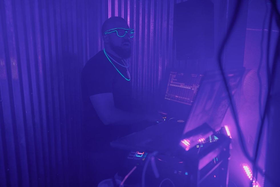 A bearded DJ behind turntables wearing glowing sunglasses