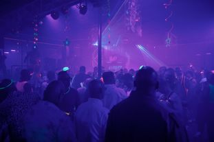 A large group of people wearing glowing clothing and accessories dancing in a club