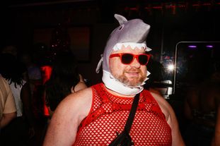 A ginger bear of a man in a mesh top and a cartoon shark mask with red sunglasses