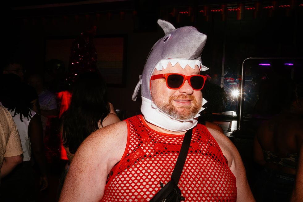 A ginger bear of a man in a mesh top and a cartoon shark mask with red sunglasses