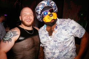 Two men on the dance floor in a club, one is wearing beach apparel and a pup-fetish mask