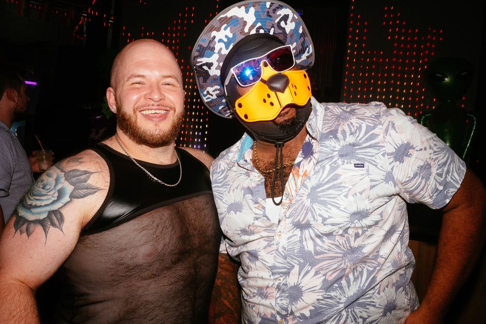 Two men on the dance floor in a club, one is wearing beach apparel and a pup-fetish mask