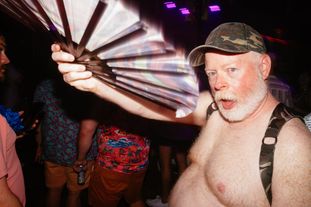 A bearded man in a camo harness and hat on the dance floor waving a fan